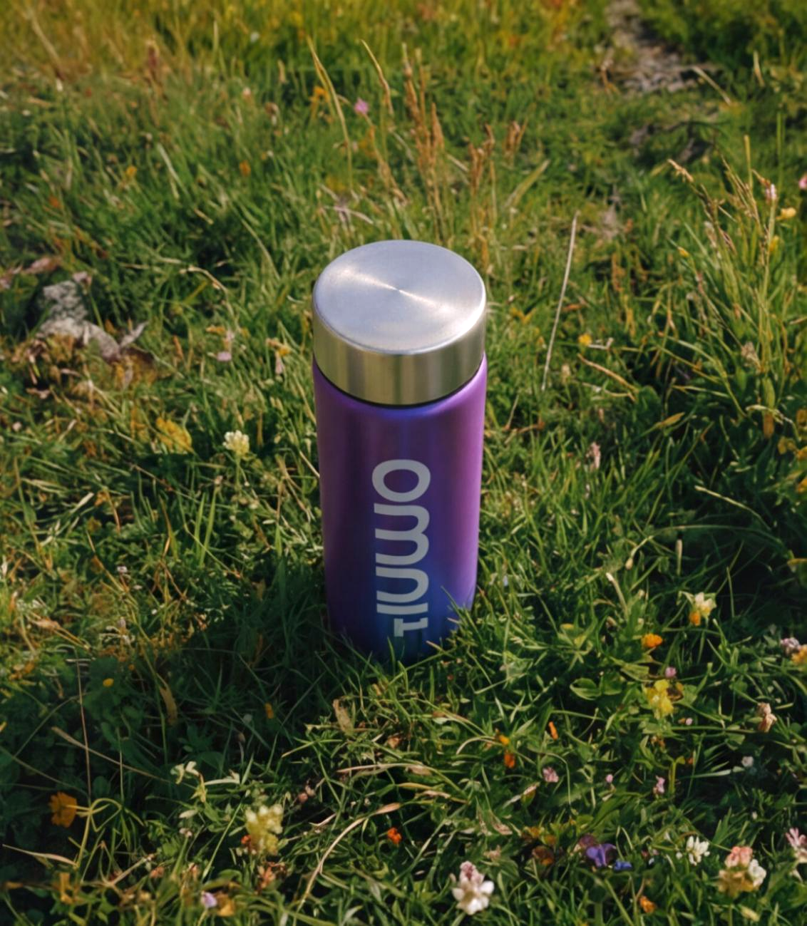 Purple OMNI¹ bottle with silver lid on grassy field with small flowers.