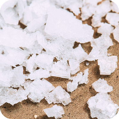 Close-up of white crystalline salt flakes scattered on brown surface.