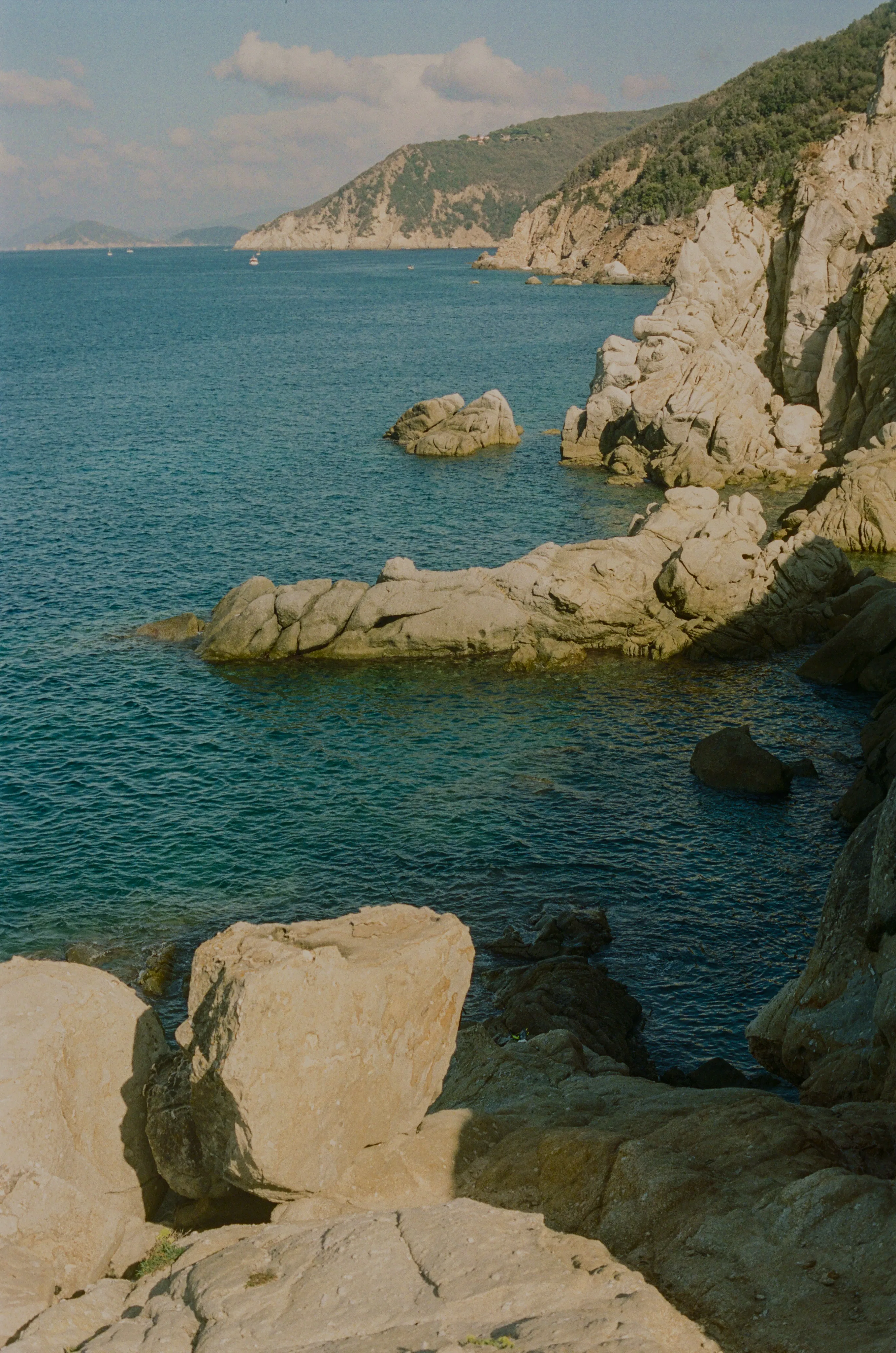 Rocky coastline with cliffs and blue sea under a partly cloudy sky.