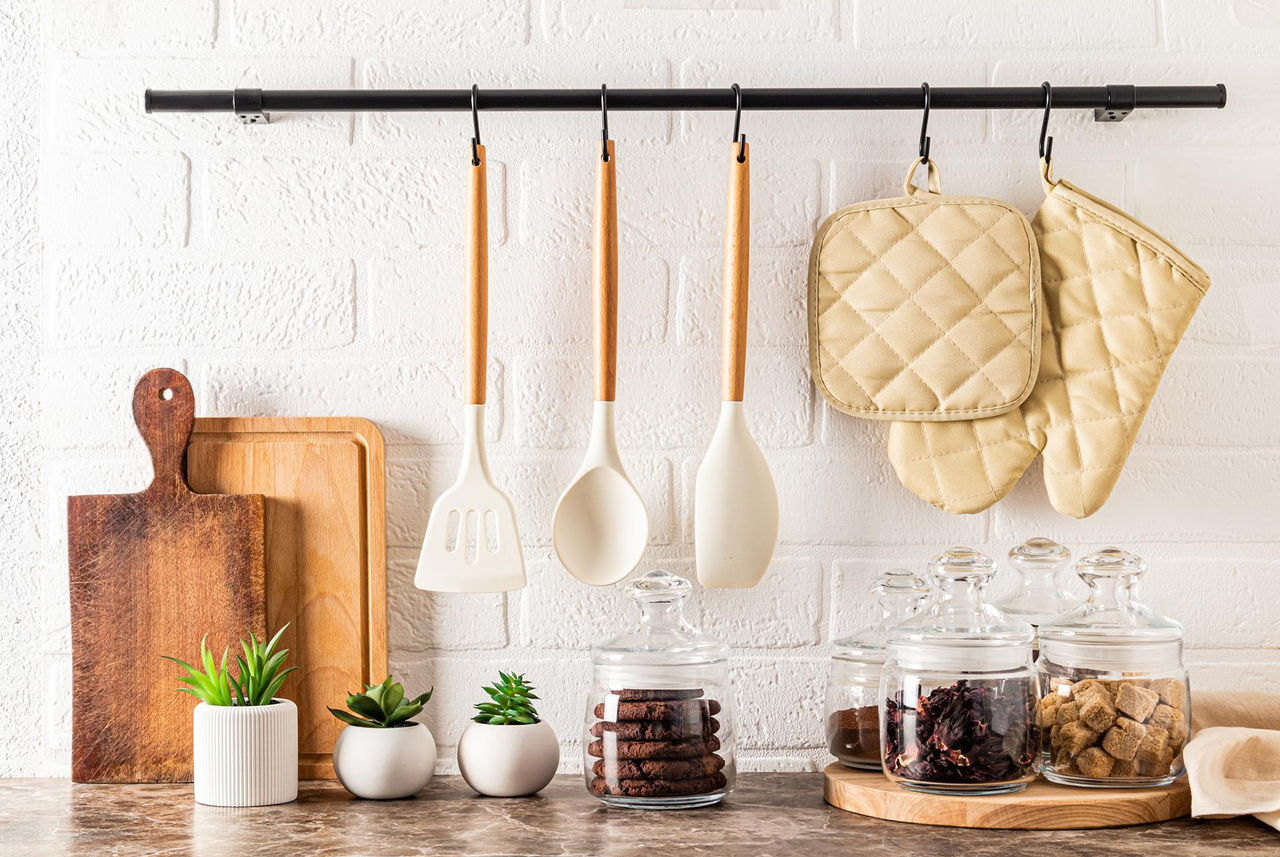 Accessori da cucina appesi al muro, tra cui mestoli, presine e taglieri: oggetti da lavare d’estate per una casa più igienica, come suggerito da Mamma Avilia.