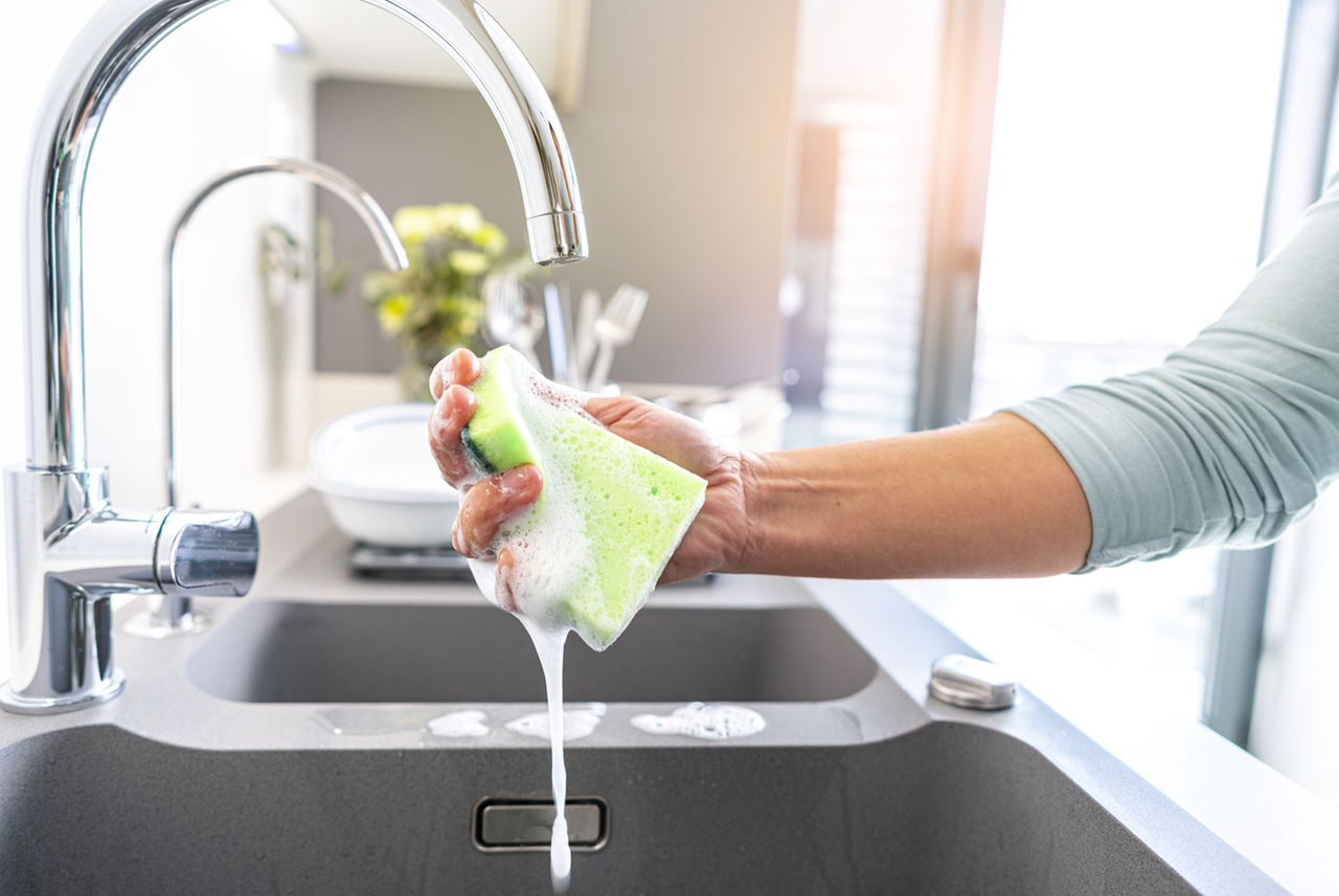 Risciacquo di una spugna insaponata sotto l’acqua corrente: il tocco finale del metodo di Mamma Avilia per igienizzare spugne e mantenere pulita la cucina in modo semplice.