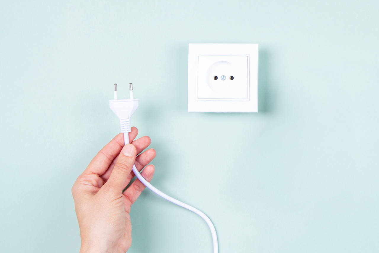 Mano che scollega una spina da una presa elettrica: un gesto semplice ma efficace di Mamma Avilia per ridurre i consumi energetici in casa.