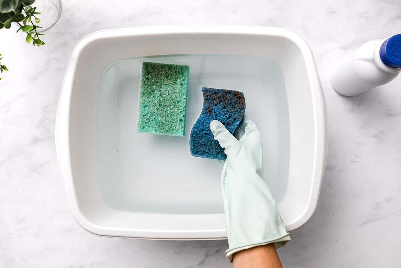 Spugne in ammollo in una bacinella con guanto protettivo: il metodo casalingo di Mamma Avilia per igienizzare le spugne in modo efficace e senza stress.