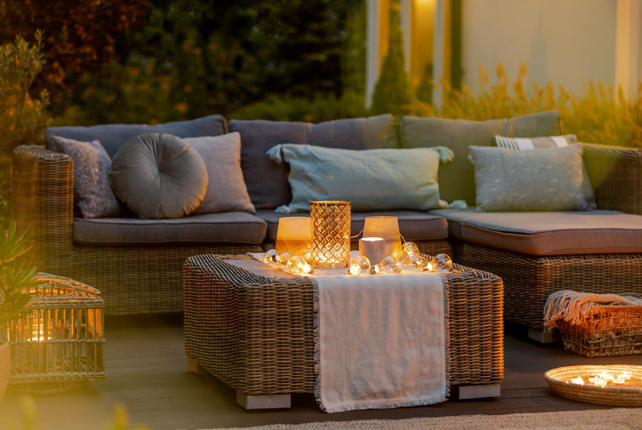 Divano da esterno con cuscini, lanterne e luci decorative al tramonto: un’atmosfera calda e accogliente secondo Mamma Avilia per rendere speciale lo spazio outdoor.