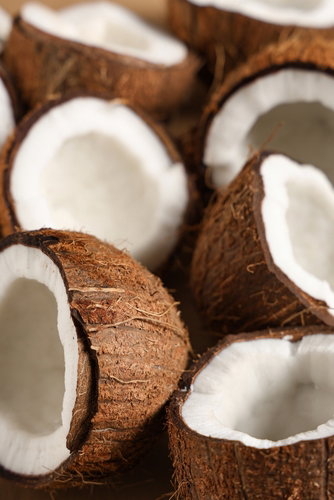 Halved coconut beside a small glass jar of coconut MCT oil
