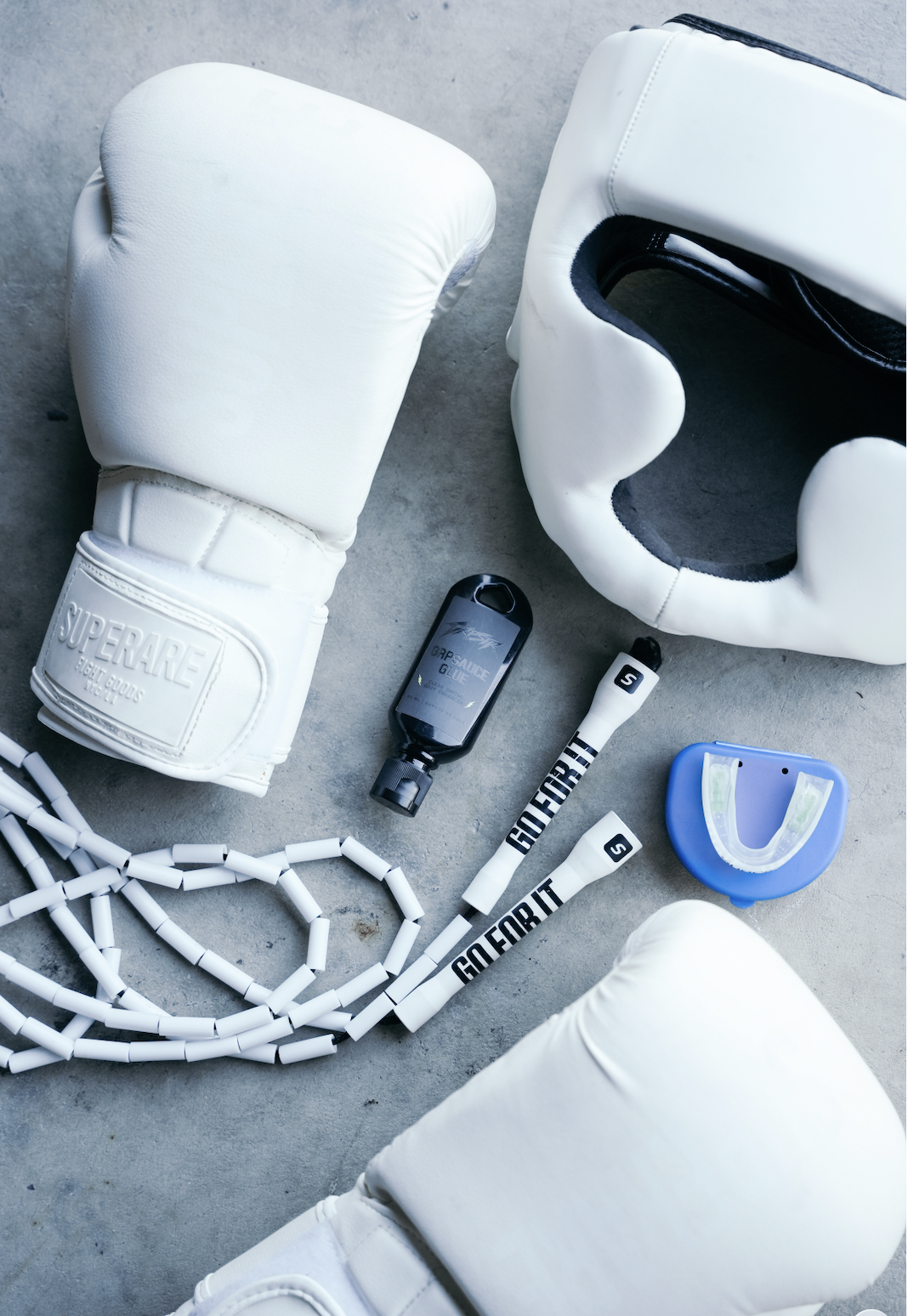 GRPSAUCE Glue bottle laid out with white boxing gloves, headgear and a jump rope on concrete