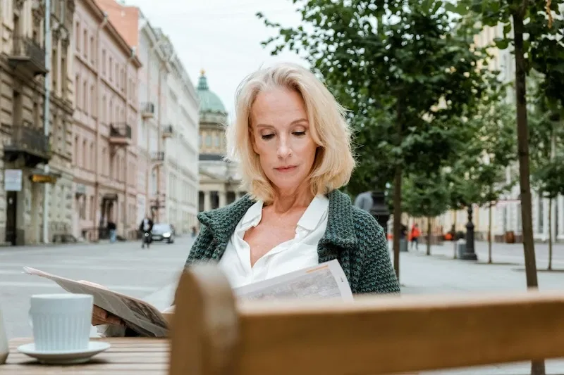 Frau, die in einem Straßencafé im Freien eine Zeitung liest.