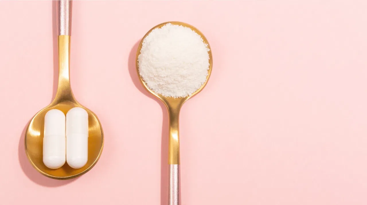 Two gold spoons on pink; one with white capsules, the other with white powder with Kollagen.