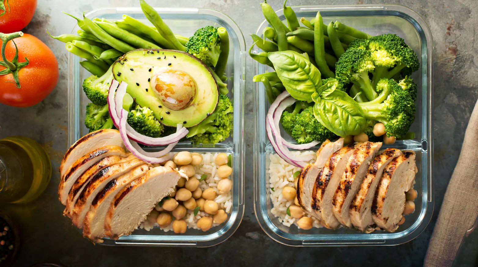 Zwei Mahlzeitendosen mit gegrilltem Hähnchen, Reis, Kichererbsen, Avocado und verschiedenen Gemüsesorten.