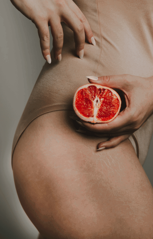 Nahaufnahme einer Person in beiger Kleidung, die eine halbe Grapefruit an ihre Hüfte drückt.