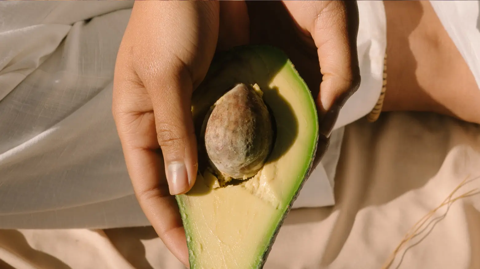 Hand hält eine aufgeschnittene Avocado, die das Fruchtfleisch und den Kern zeigt.