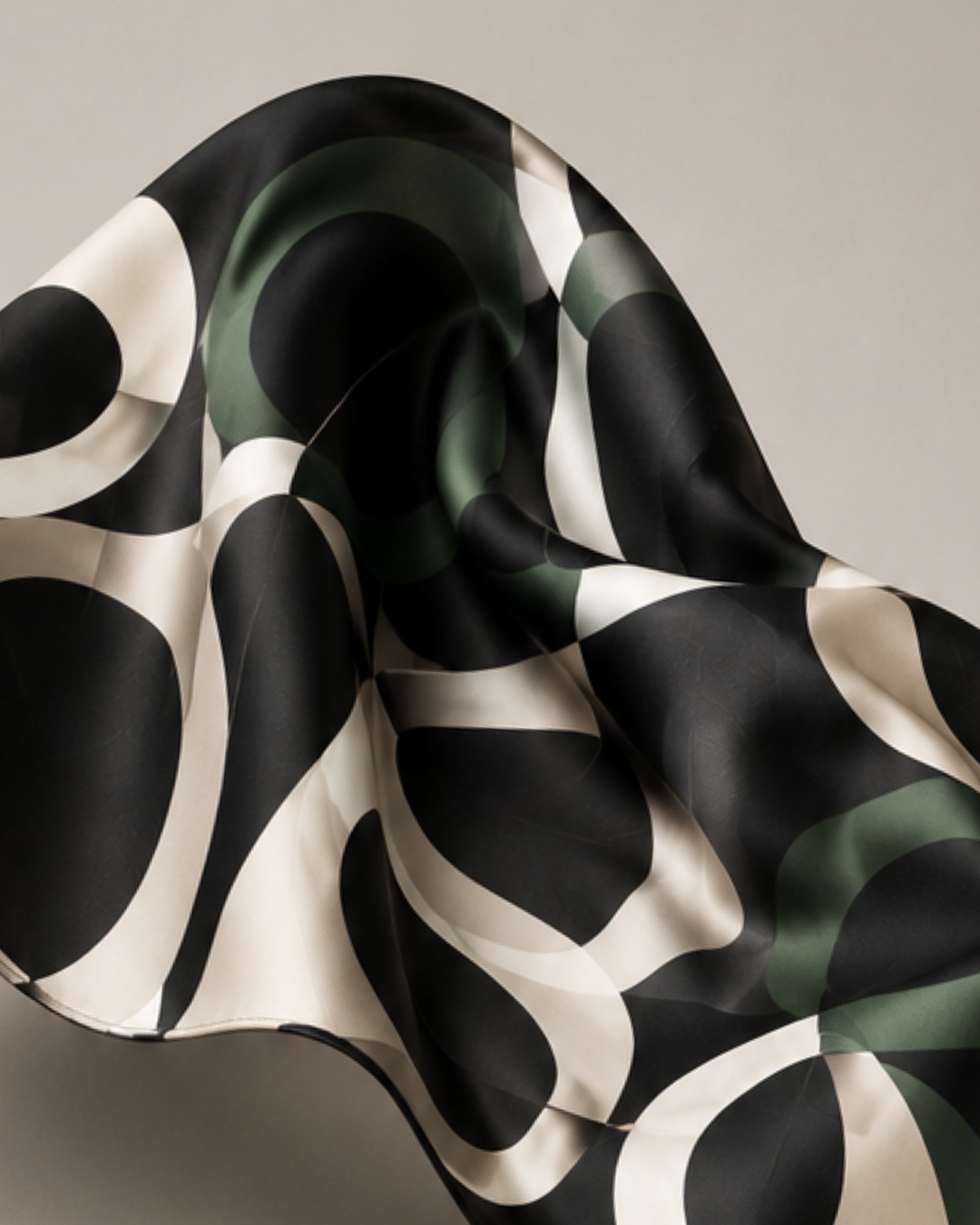Close detail of the Italian silk twill in motion — overlapping ovals in black, ivory and forest green