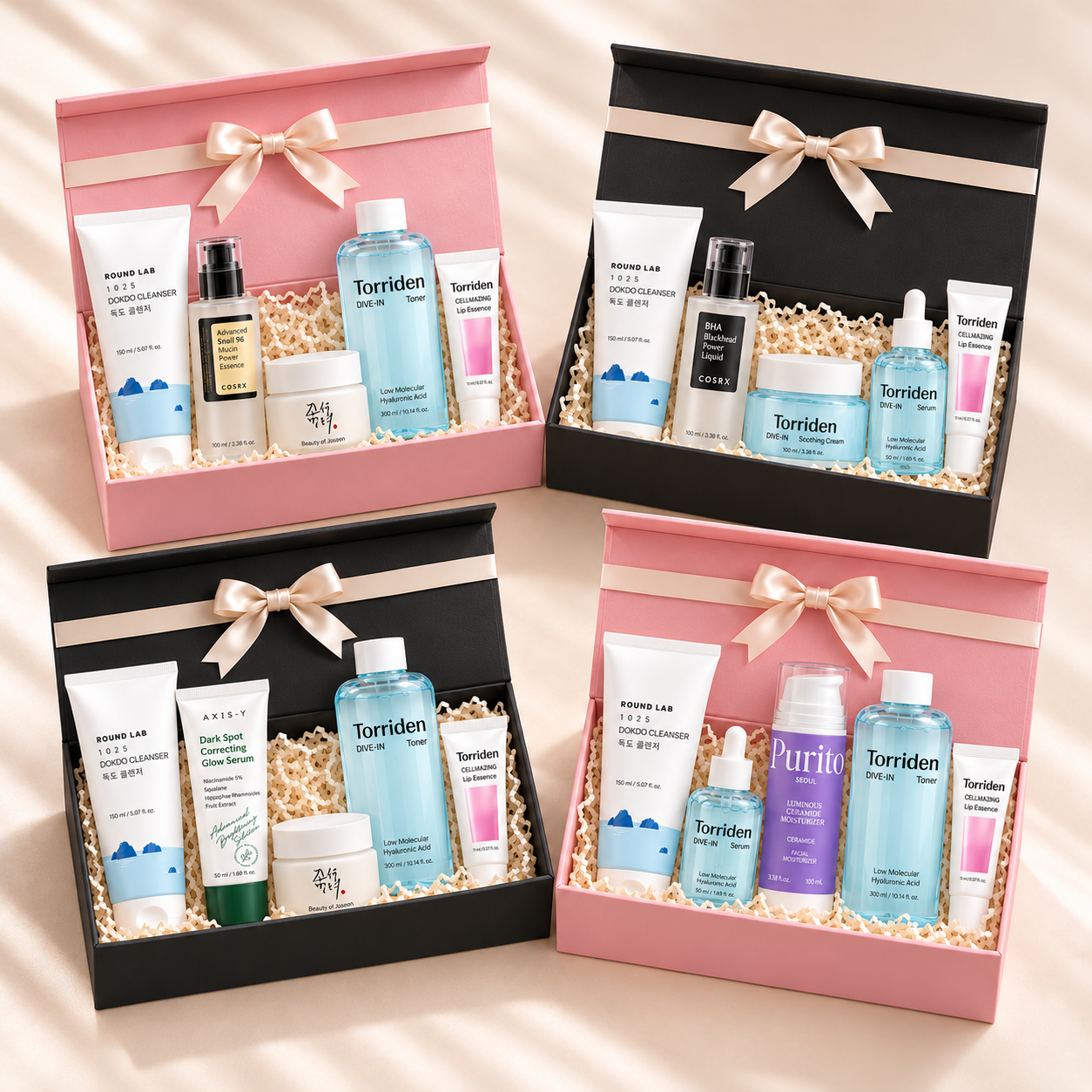 Four AERI gift boxes, two pink and two black, each tied with a cream satin bow and filled with Korean skincare from Round Lab, COSRX, Torriden, Beauty of Joseon, AXIS-Y and Purito