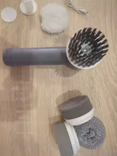 La brosse électrique coloris argent posée au sol avec sa tête à poils, ses disques et son câble de recharge