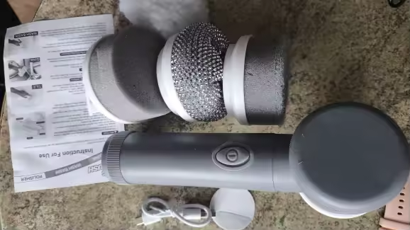 Photo envoyée par un client : la brosse de nettoyage argentée posée sur un plan de travail avec ses têtes de brosse, son câble de recharge et la notice d'utilisation
