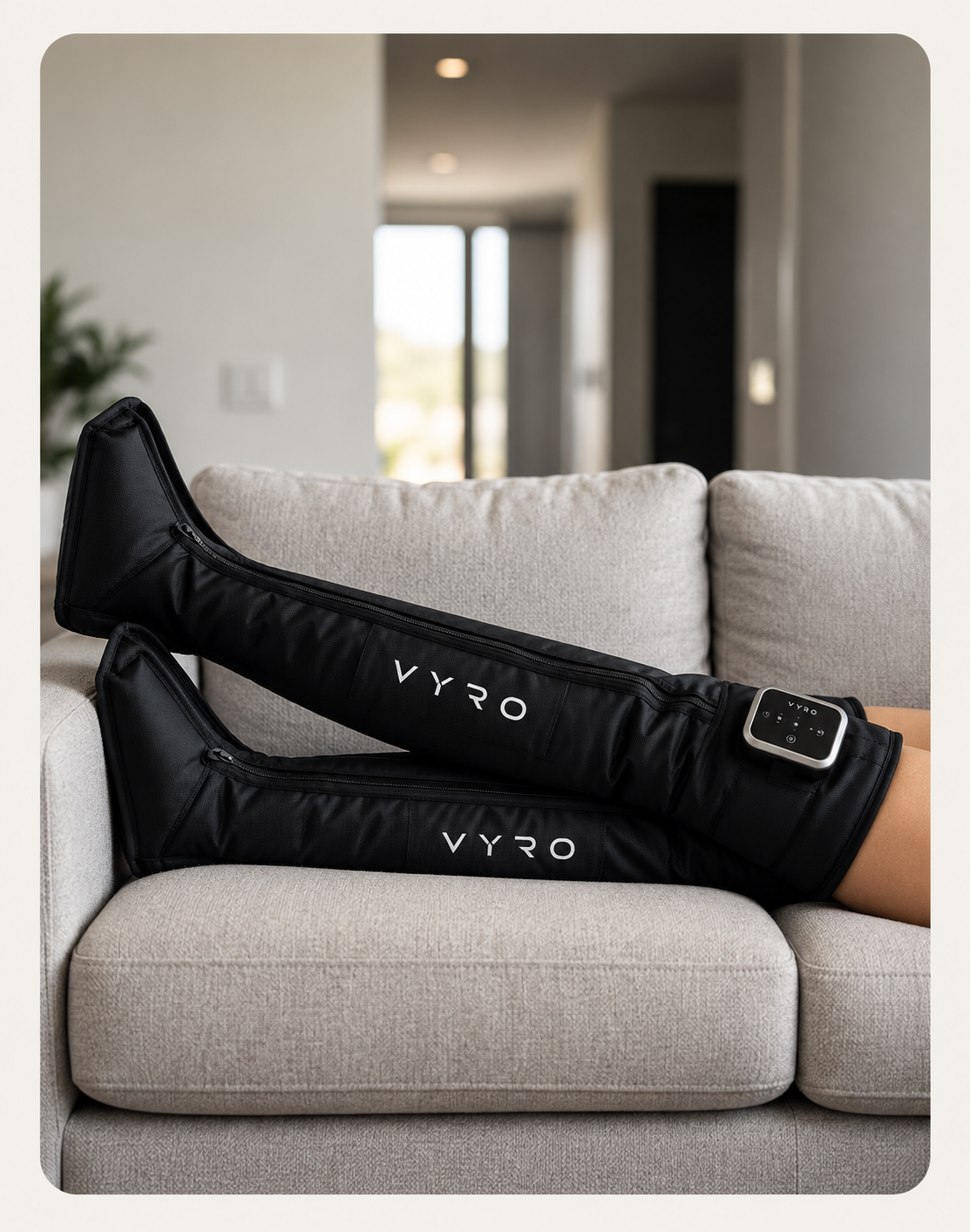 Legs raised on a grey sofa wearing VYRO compression boots with the controller at the thigh