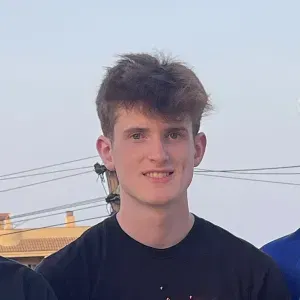 Young man with short brown hair wearing a black shirt, outdoors with a clear sky background.