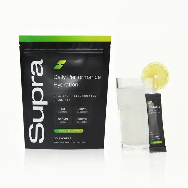 Black Supra creatine and electrolytes hydration drink mix pouch, a glass with lemon lime drink, and a supplement sachet.