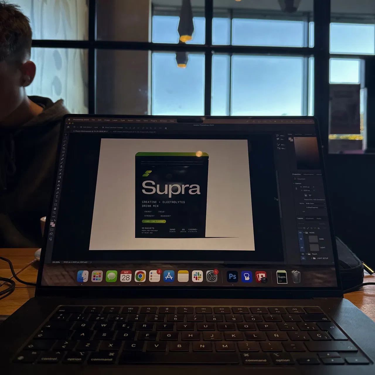 Laptop screen displaying a design of a Supra creatine electrolytes drink mix pouch in a cafe.