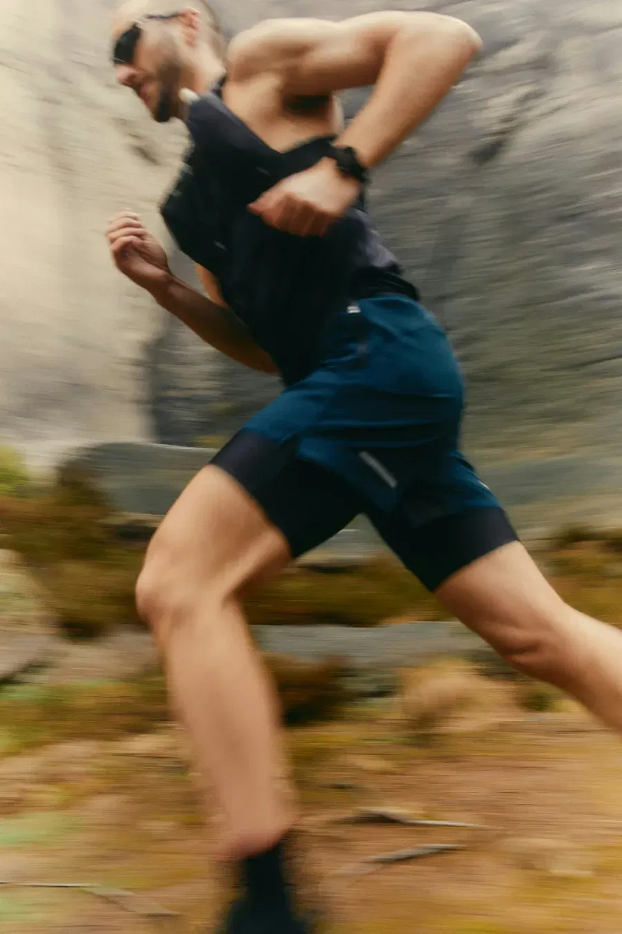 Runner wearing sunglasses and athletic gear sprinting outdoors on rocky terrain.