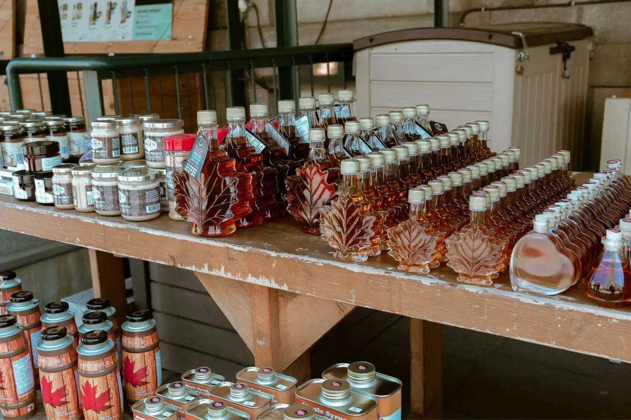 Bottles and jars of maple syrup on a wooden table, featuring leaf-shaped bottles.