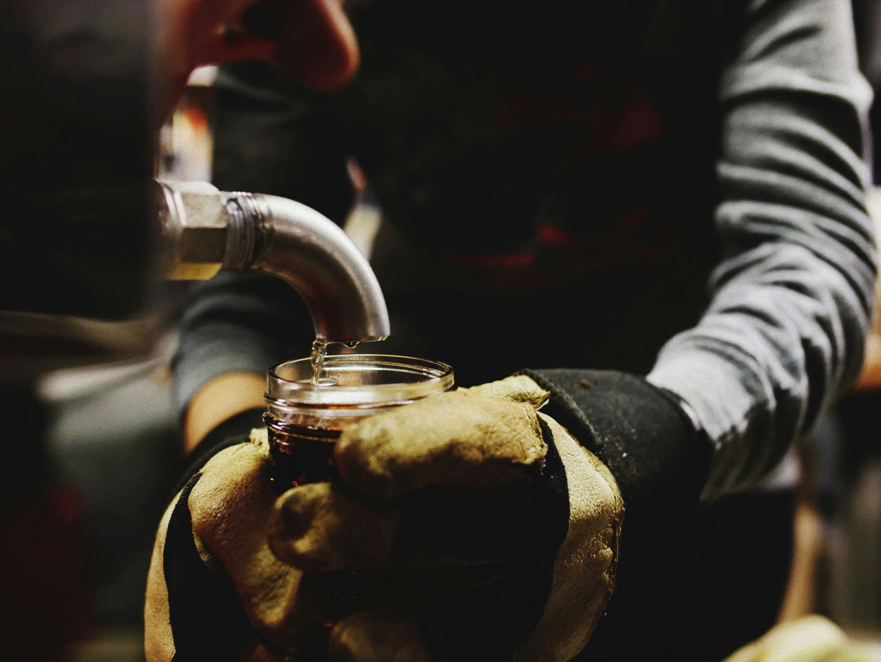 Hands holding cup getting maple syrup from barrel 