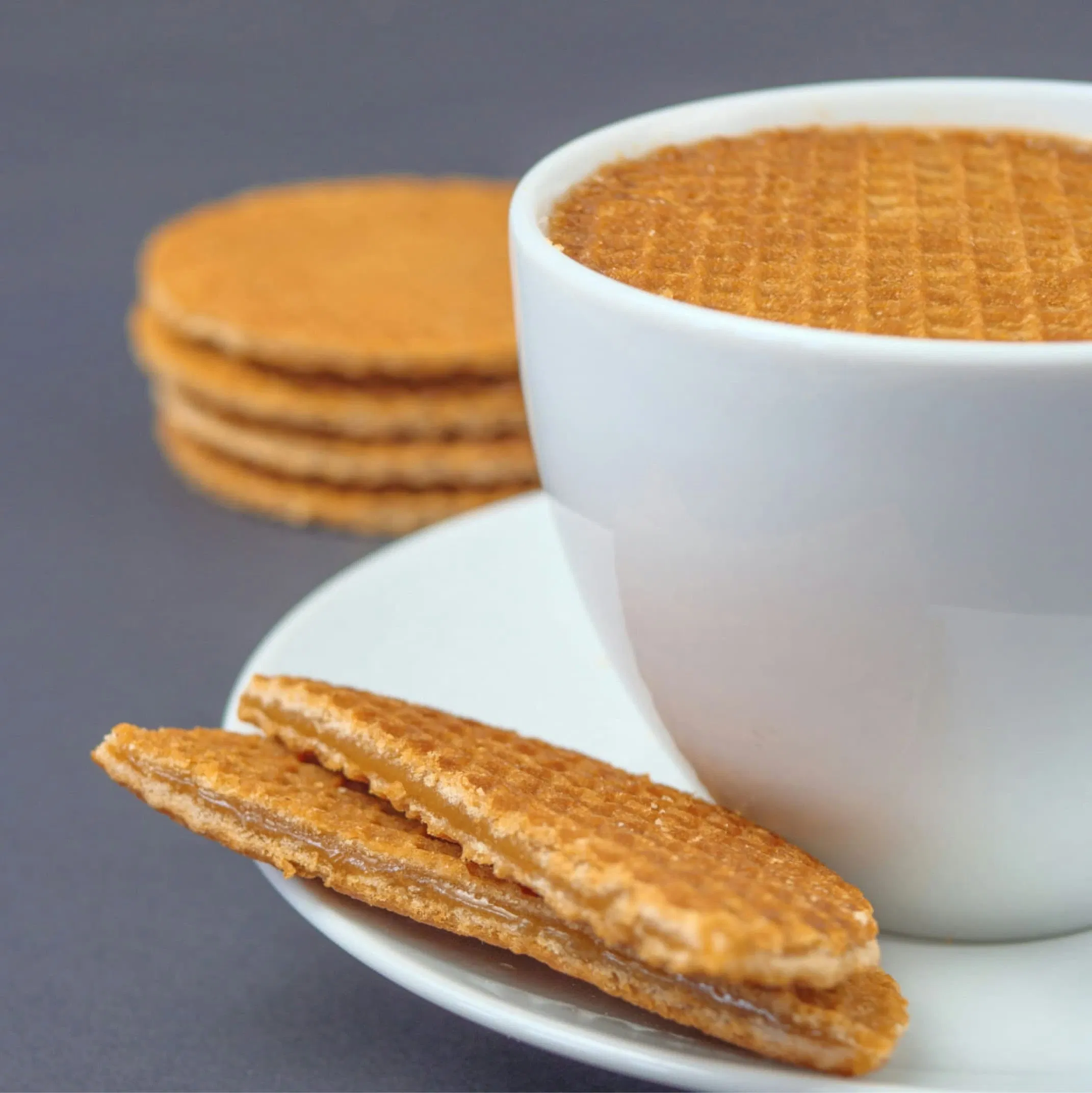 A white cup of coffee with a stroopwafel on top, surrounded by more stroopwafels on a plate.