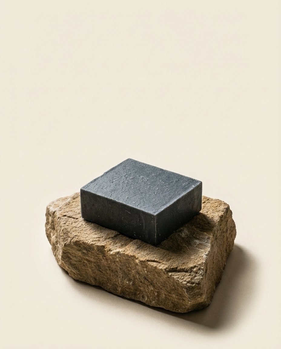 Black soap bar sitting on a rock against a pale cream background