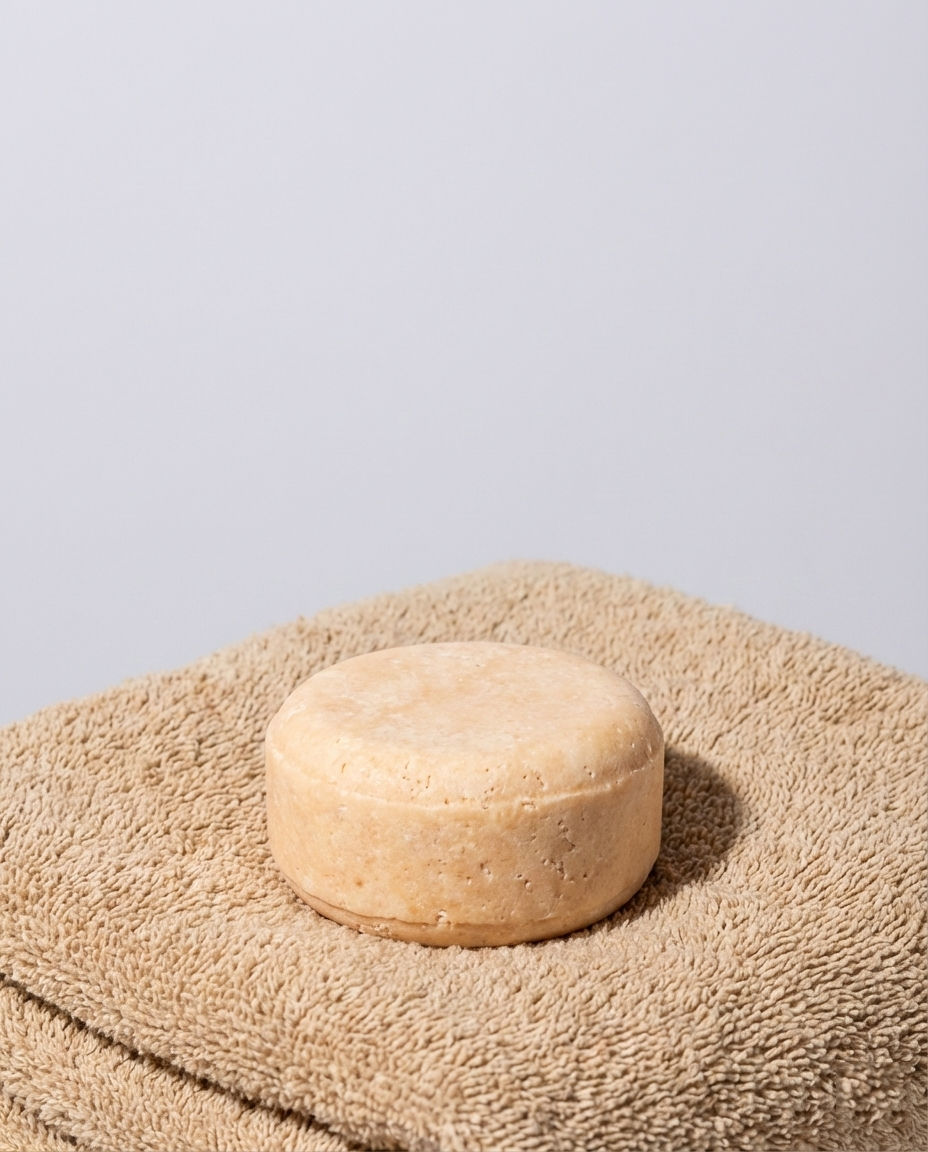 Round orangey soap bar resting on sandy coloured towels against a grey background
