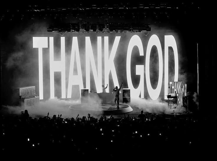 The Kid LAROI on stage in black and white in front of a giant THANK GOD screen, crowd in the foreground