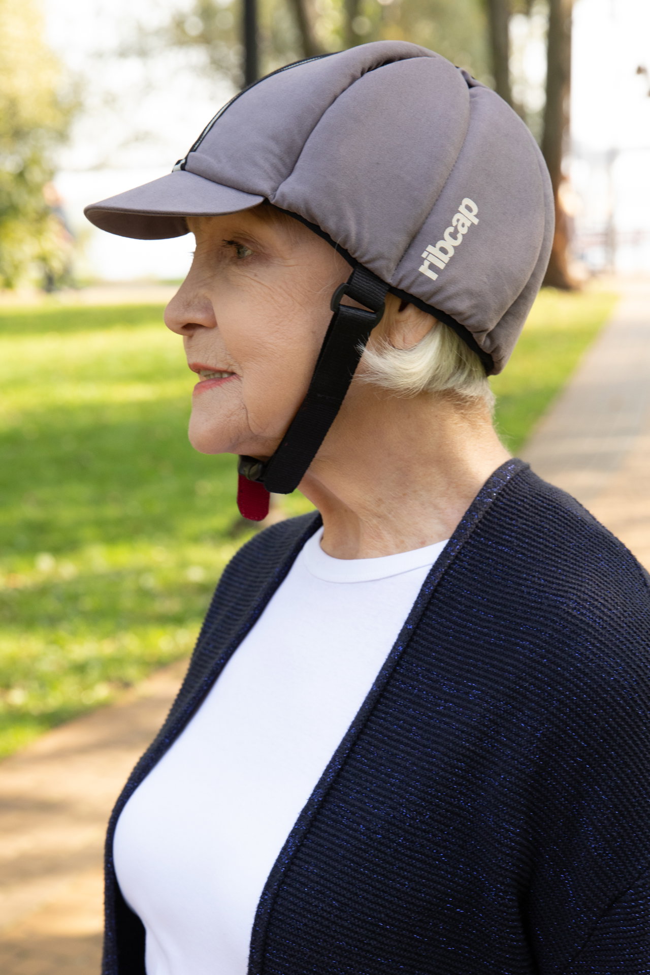 Side profile of an elderly woman outdoors wearing a gray protective cap with a chin strap