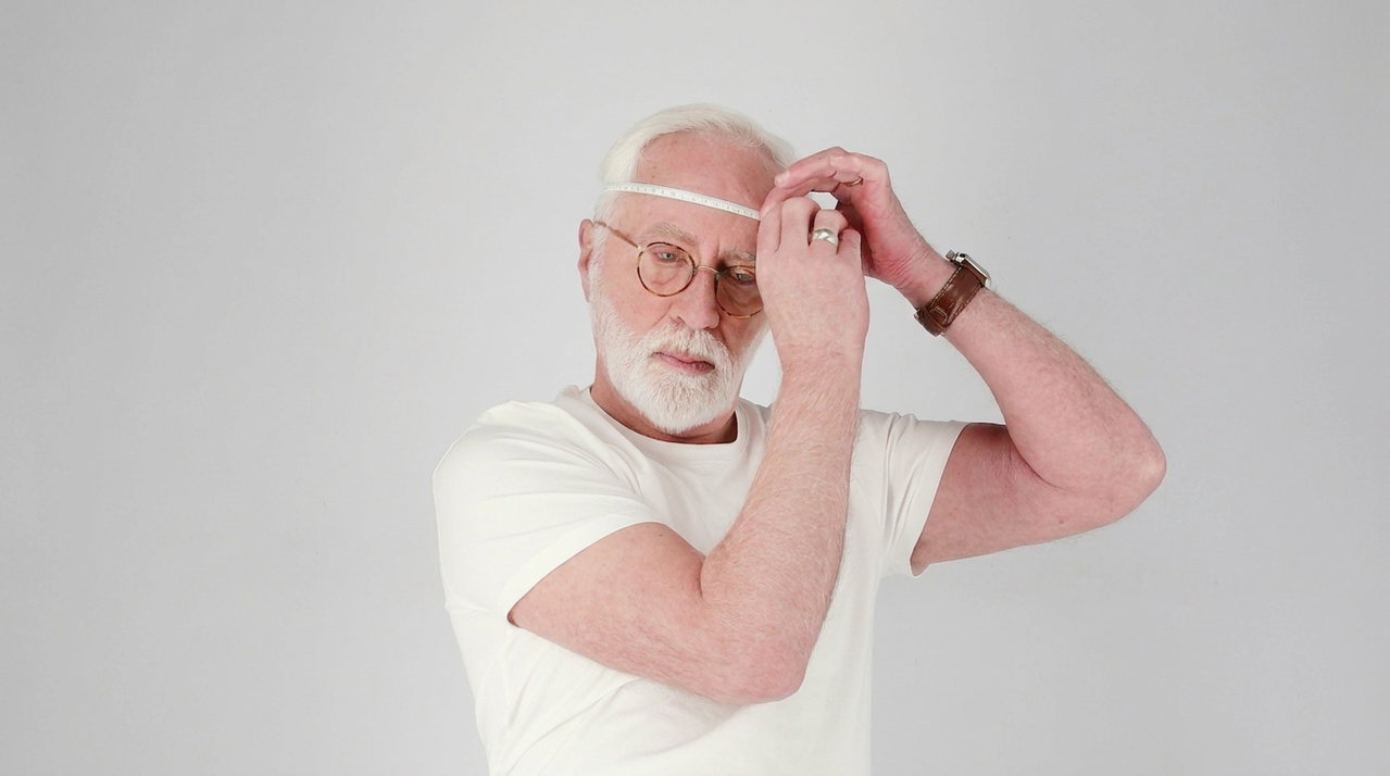 Older man wearing glasses measuring his head with a measuring tape