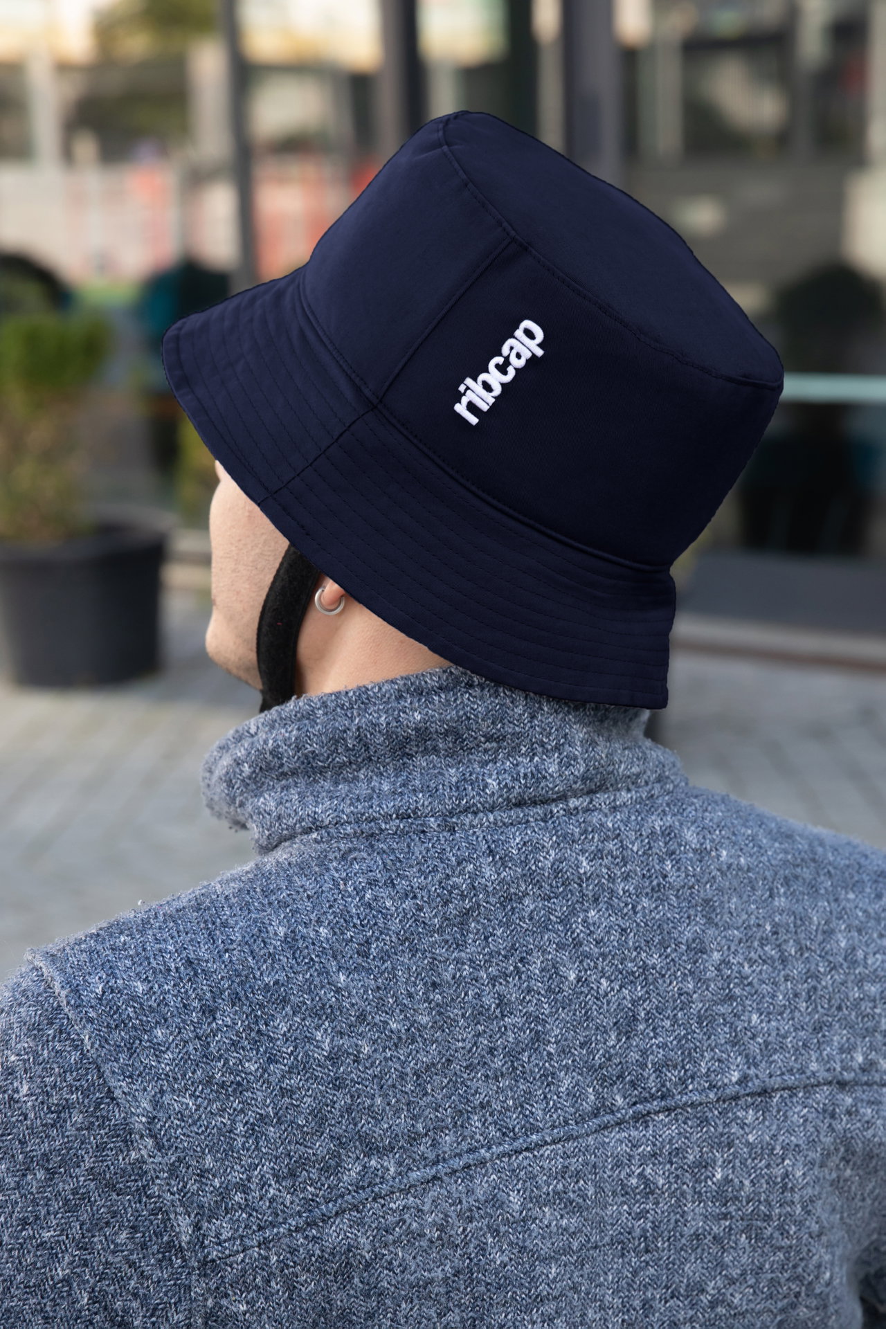 Back view of person in gray sweater wearing navy blue bucket hat with strap outdoors