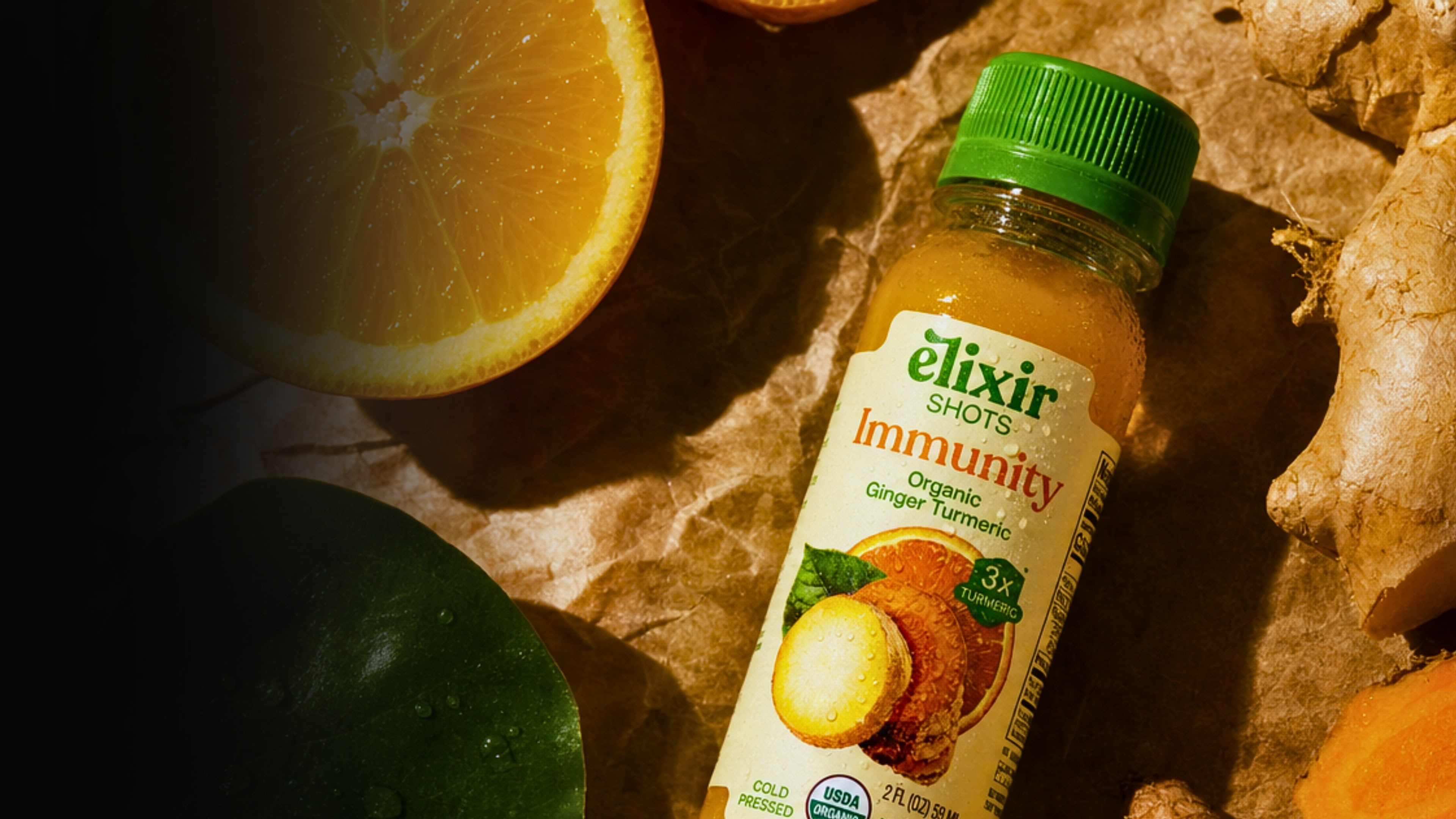 An Elixir Shots Immunity bottle resting on parchment with fresh orange slices, ginger root and turmeric