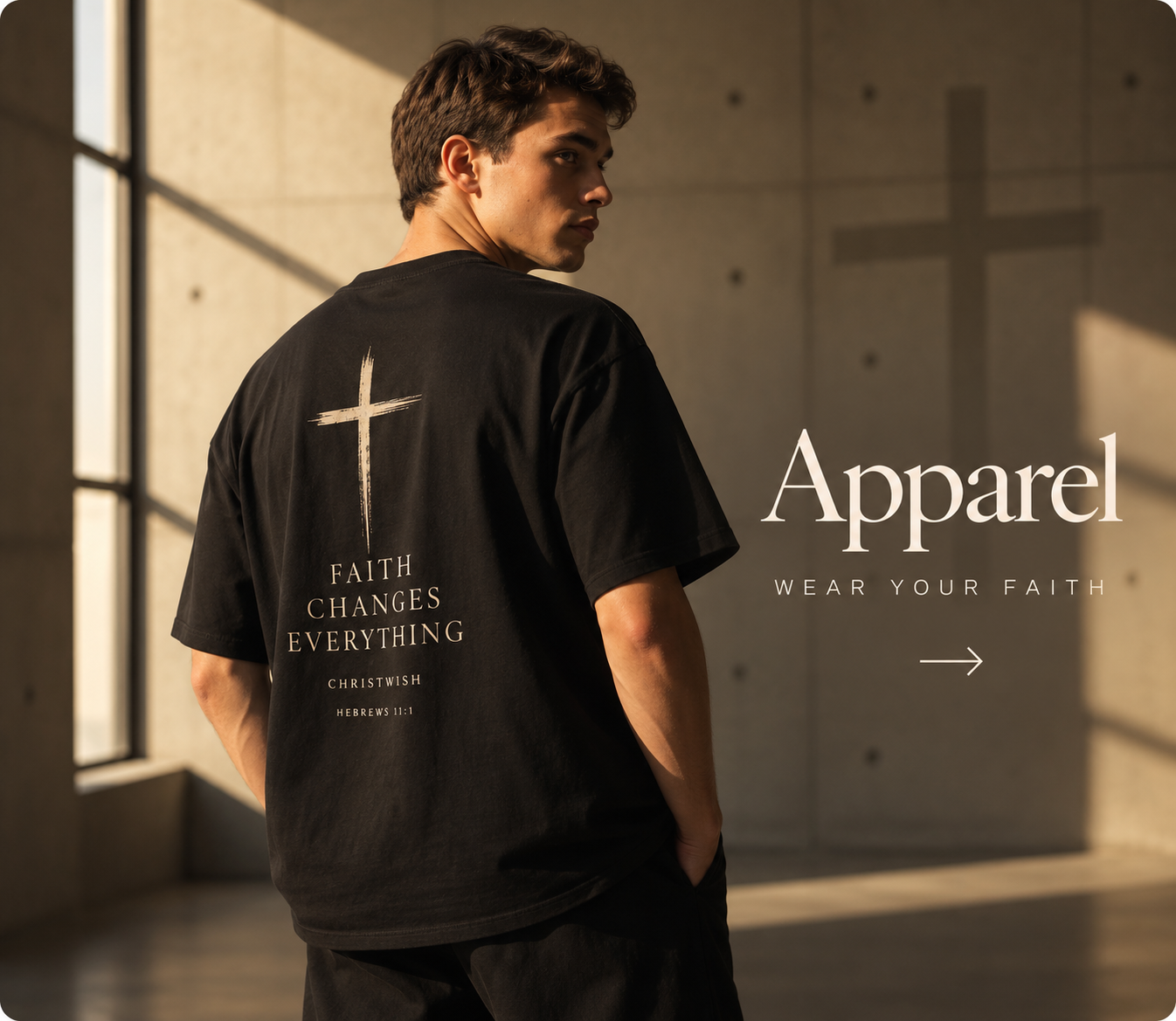 A man wearing an oversized washed-black t-shirt in a sunlit minimal concrete space