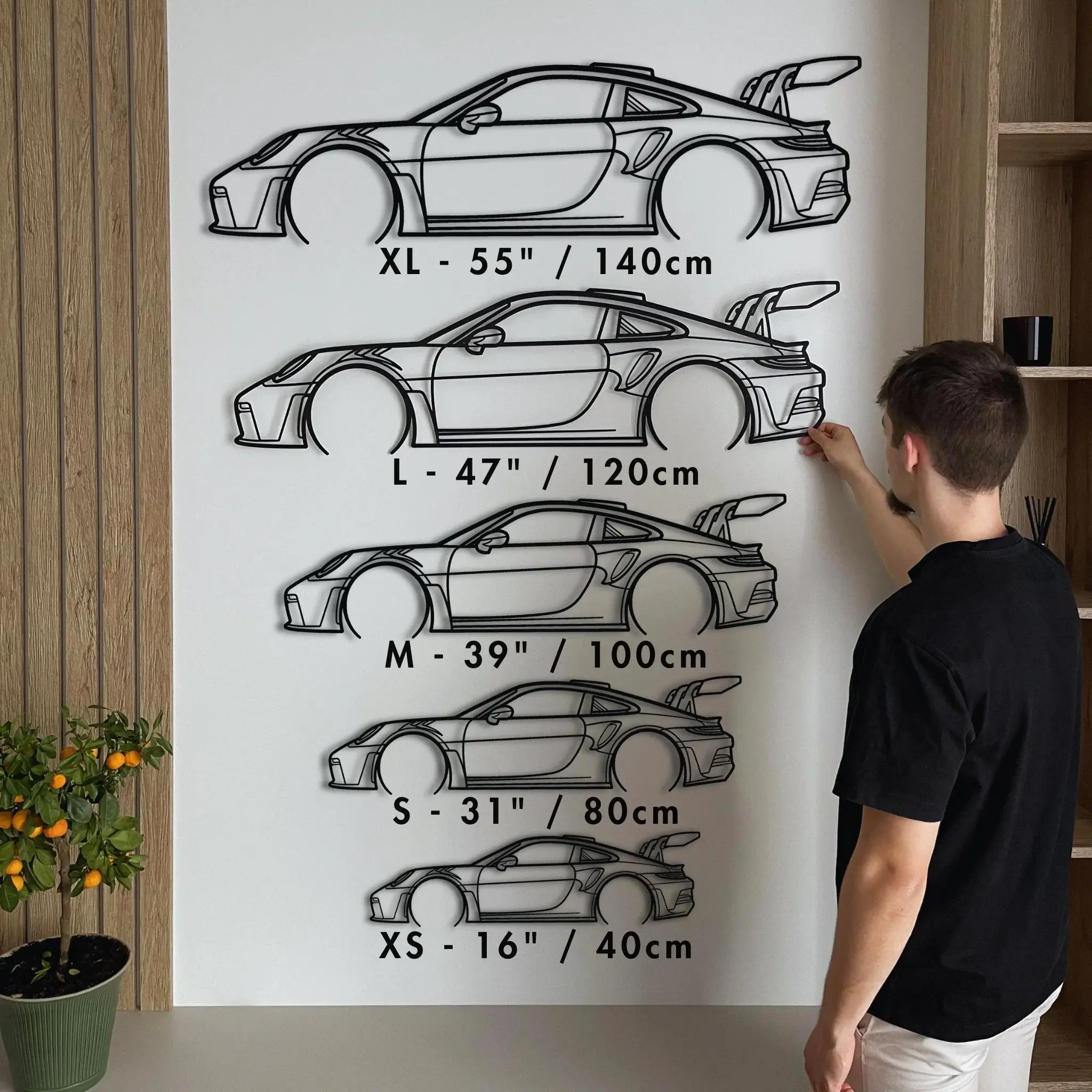 Man hanging Porsche steel silhouettes in five sizes from XS to XL on a white wall