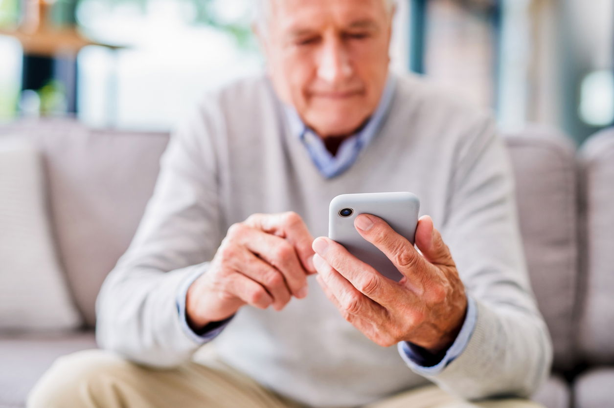 Older adult using a smartphone, sitting on a couch.
