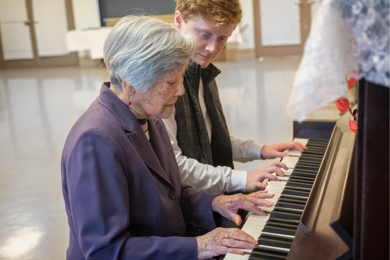 Dementia patient doing music therapy with a teacher sitting at a piano.
