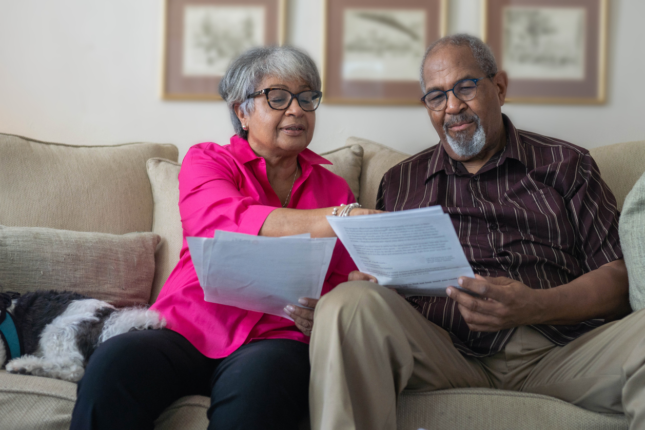 Older senior adults sitting on a couch looking at reminders and messages on a piece of paper.
