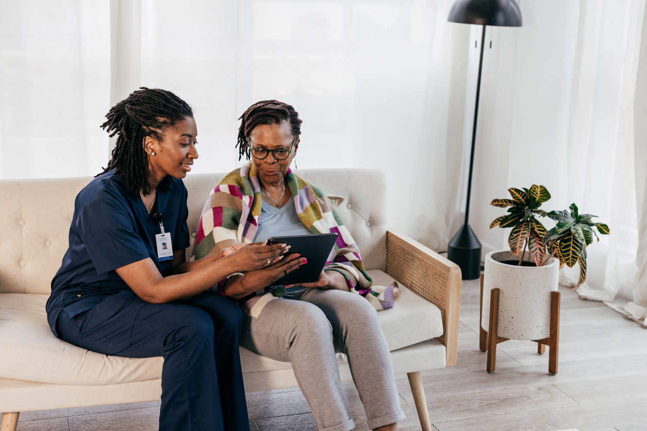 Caregiver showing off a technology solution to an older adult on a couch in a living room.