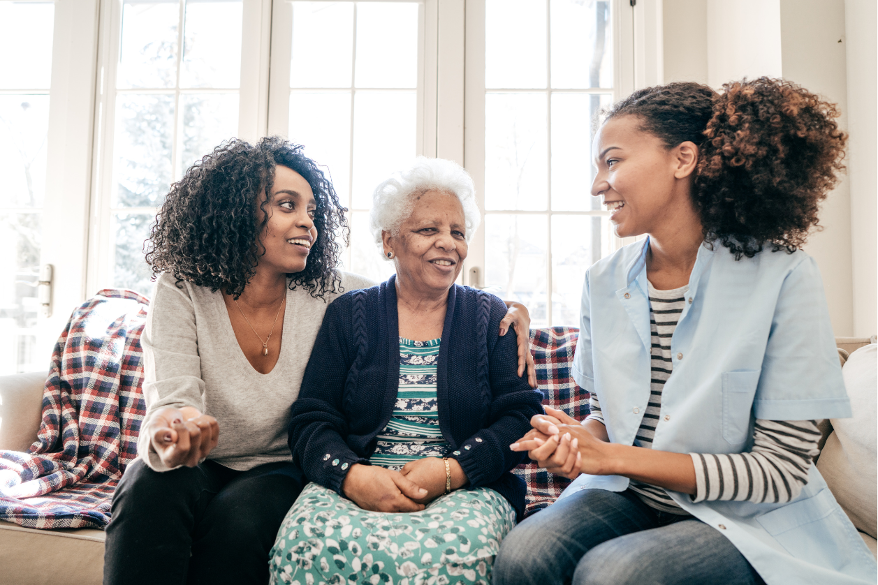 Two women with grandma who has memory loss providing emotional support in a living room.