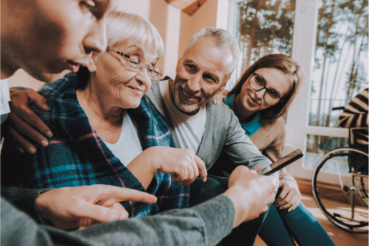 Family is gathered around a living room helping older adult with memory loss use new tech.