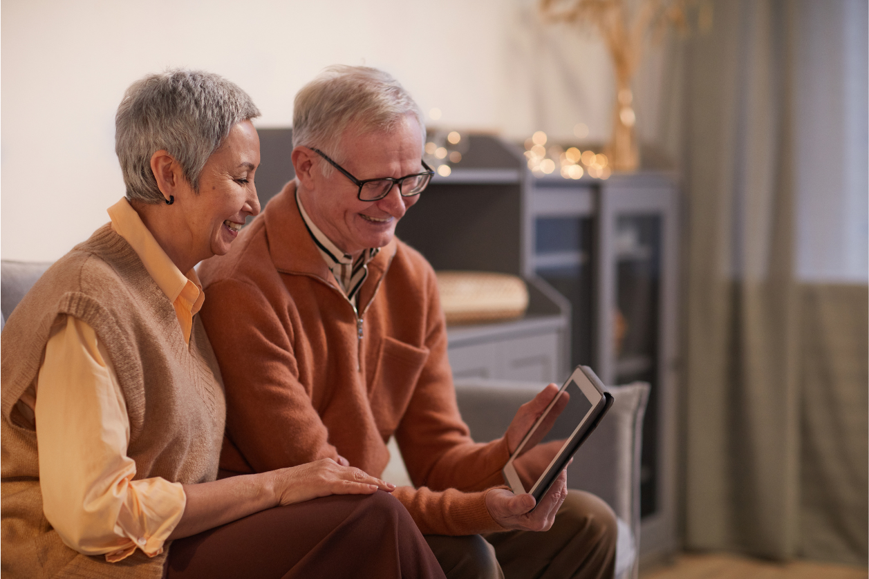 A man with dementia and a woman sitting in living room looking at a digital board with reminders.