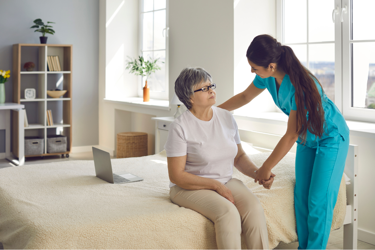 Older adult with dementia sitting on a bed with a caregiver going through daily routine.