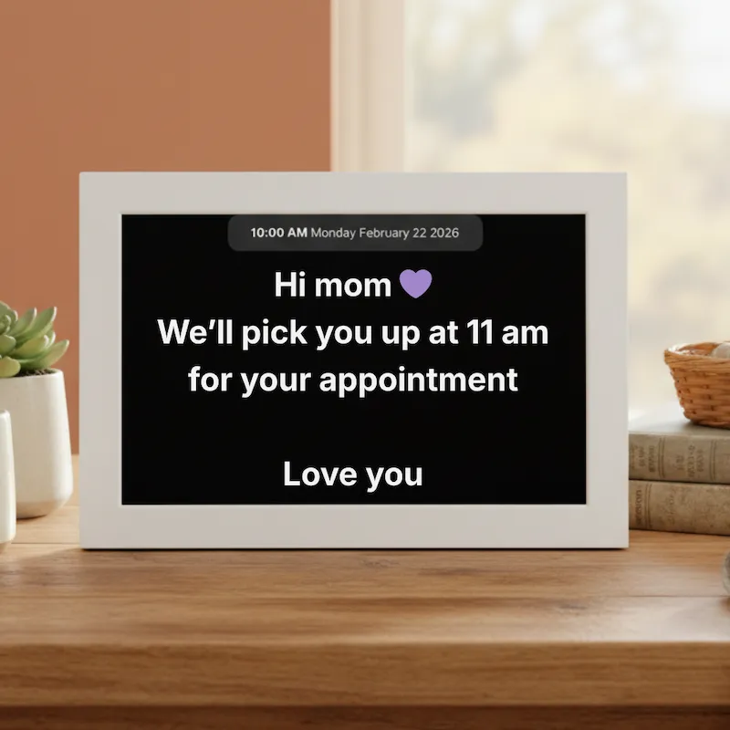 Memoryboard dementia clock and digital reminder display showing a message from family on a bedside table for a loved one with memory loss
