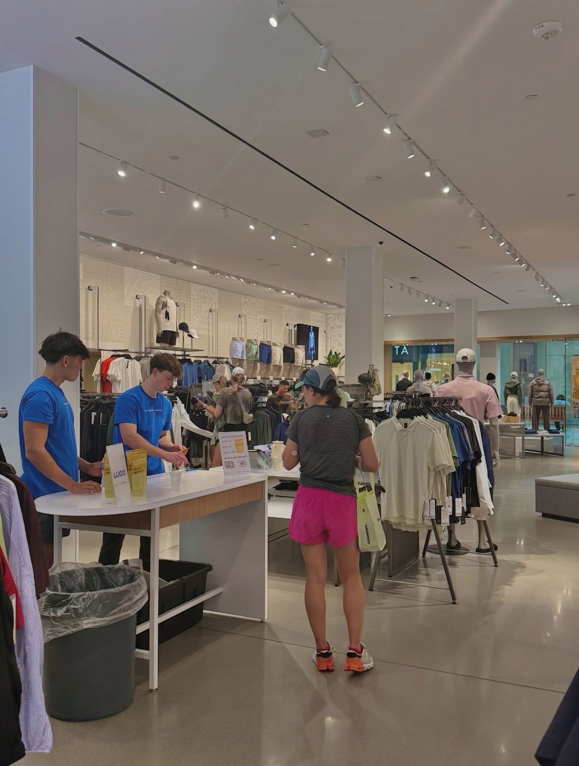Shoppers and staff inside a bright clothing store with racks and displays of apparel.