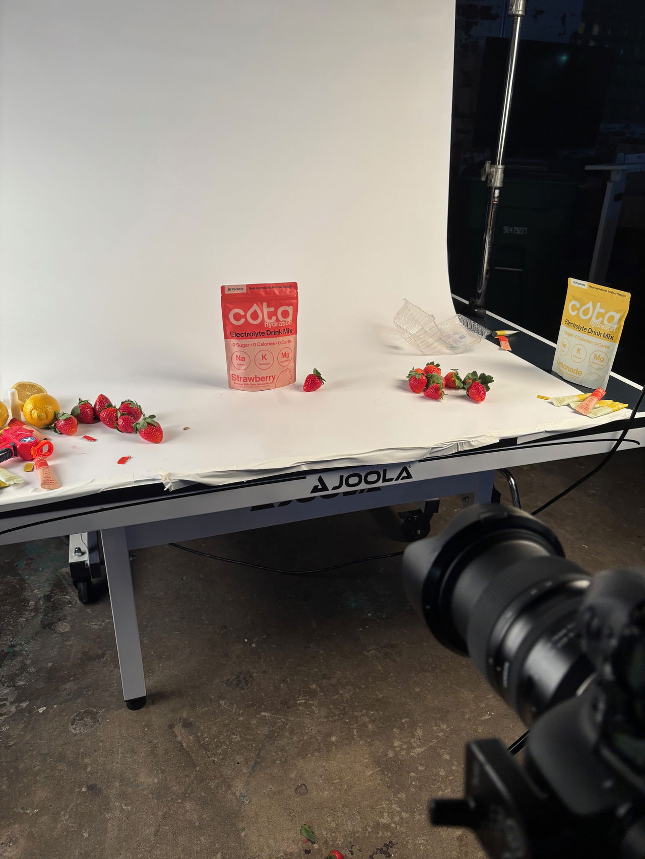 Strawberry electrolyte packet on table with white background with camera in front in photoshoot setting.