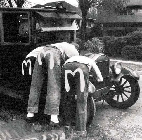 Evisu campaign image: two men in work shirts bent over the engine of a vintage car, the white Evisu seagull motif hand-painted on the back pockets of their jeans, shot in black and white