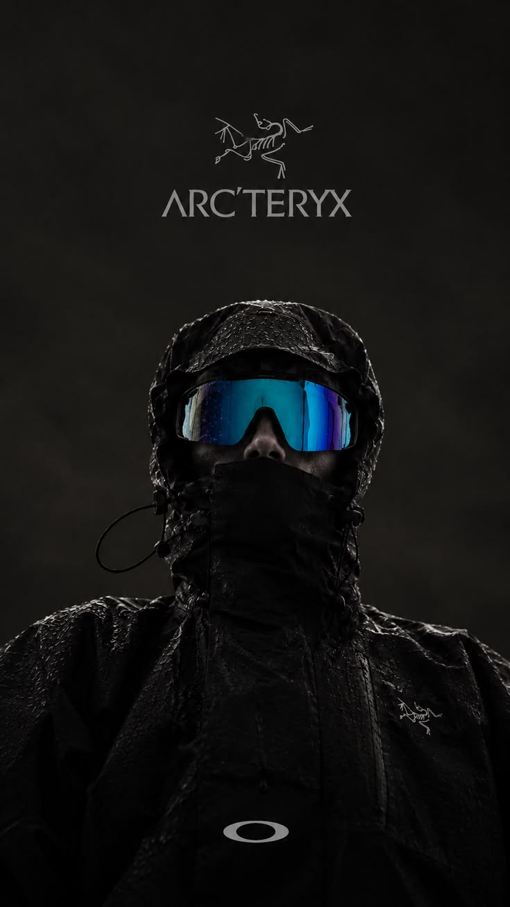 Arc'teryx campaign portrait: a figure in a rain-soaked black hooded Arc'teryx shell with the collar zipped high and blue mirrored goggles, shot from below against a dark backdrop under the Arc'teryx logo