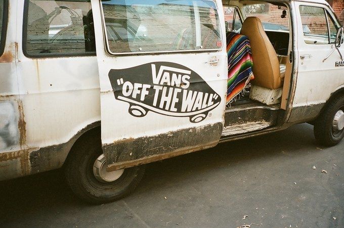Vans campaign image: a weathered white van with its side door open, showing a large Vans Off The Wall logo and a striped blanket on the seat inside